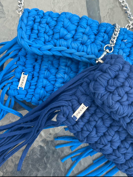 Blue crochet handbag with tassels on a grey surface