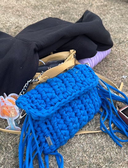 Blue crochet bag with tassels on a surface